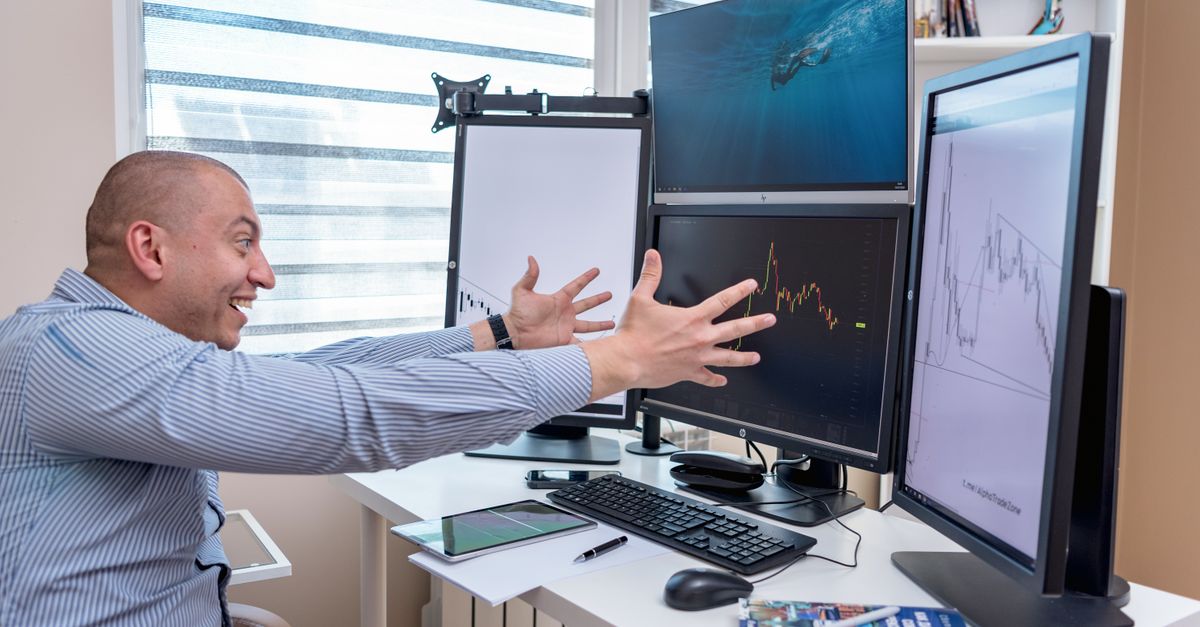 A forex trader's desk with MetaTrader charts open on multiple monitors